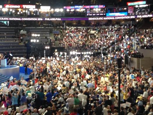 Delegates crowd the stage at the Democratic National Convention, many carrying signs that say 