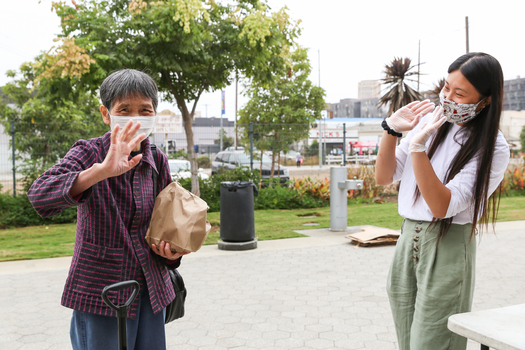 A local resident waves as she picks up her bag of produce from the Chinatown Health Initiative at the Los Angeles State Historic Park. (Veronica Monjara/Las Fotos)