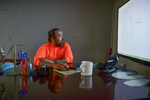 Facilities manager Wes Davis at Turtle Mountain Community College is at work at his desk. A miniature wind turbine sits on its surface. (Photo by Jessica Plance/Homegrown Stories)