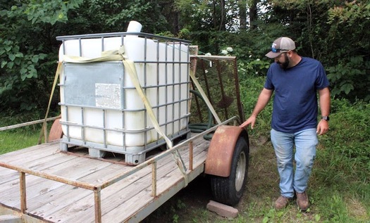 Garrett Betts inspects his 275-gallon tank and trailer setup. Before Garrett built the trailer, he was hauling water with the tank in the bed of his truck.(Photo by Zachary Shephard)