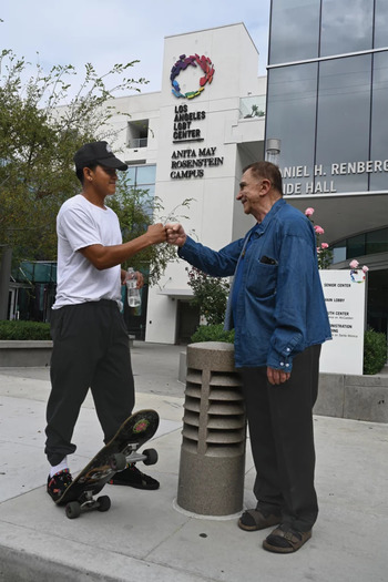 Carlos J. Mejia Vijil, 23 (left), and John Maragioglio, 82, share a bonding moment outside the Anita May Rosenstein campus, where Maragioglio lives in senior housing. Mejia Vijil lived in the youth housing on the campus before getting his own apartment. (Francesco Da Vinci/YES! Media)