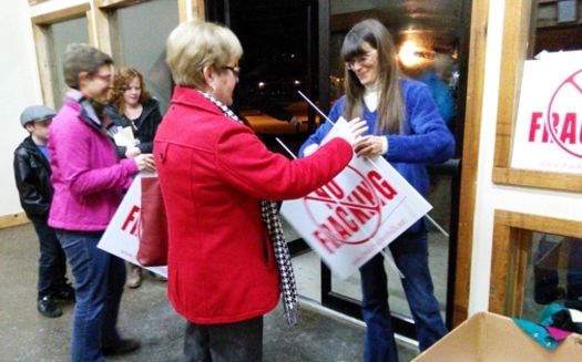 PHOTO: A citizen picks up a sign in opposition to hydraulic fracking in Kentucky as she leaves an informational meeting about the technology. Photo by Greg Stotelmyer.