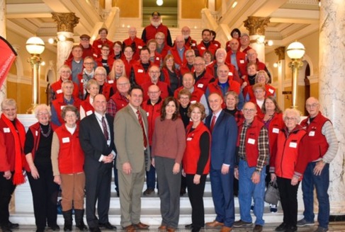 Clad in their signature red vests, members of AARP South Dakota shared their priorities with Gov. Kristi Noem, front row center, during Lobby Day at the State Capitol. (aarp.org/sd)