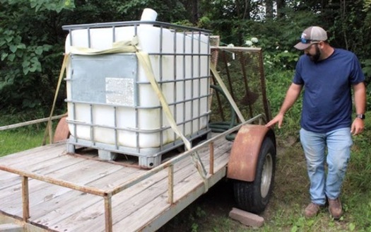 Garrett Betts inspects his 275-gallon tank and trailer setup. Before Garrett built the trailer, he was hauling water with the tank in the bed of his truck.(Photo by Zachary Shephard)